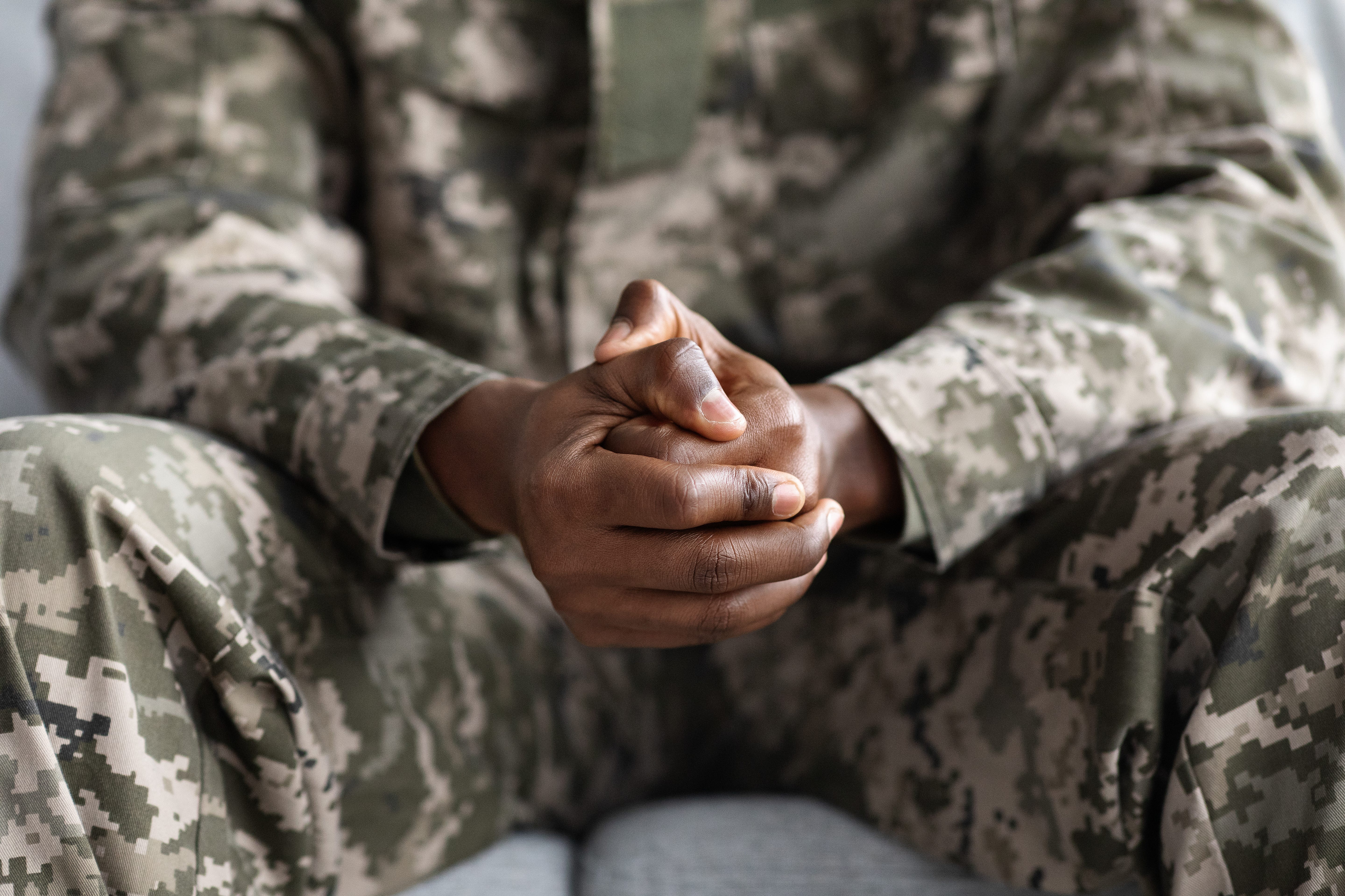 Military service man sitting down with hands folded together.