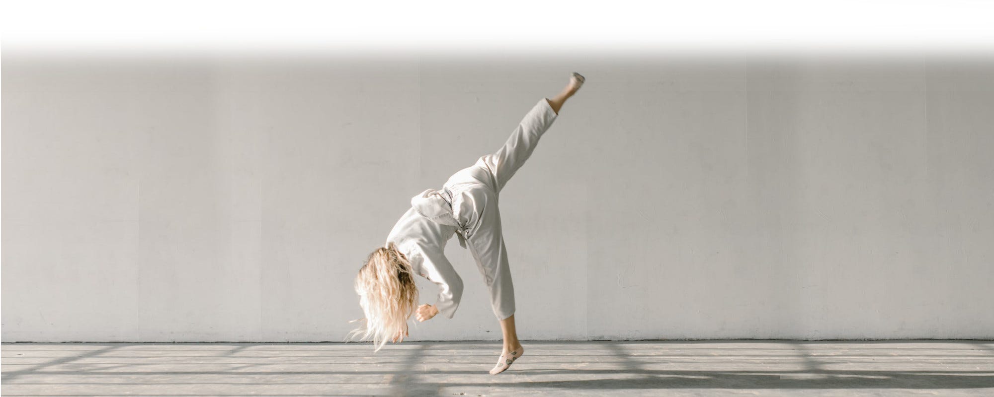 A woman in a karate outfit spin kicking upside down in the air