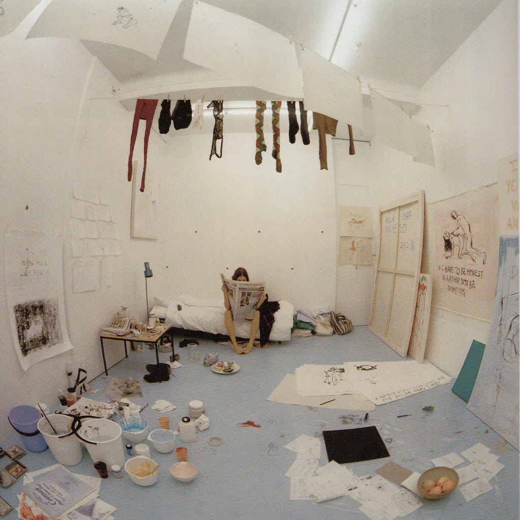 Artist Tracey Emin sits on a cot in a white room, her art studio, where she is nude and reading a newspaper. Her laundry is drying from the ceiling beside sketches hanging on clothespins and the floor of the studio is covered with the detritus of painting: canvases, paints, as well as the stuff of everyday life, as if she has been living here, cloistered.