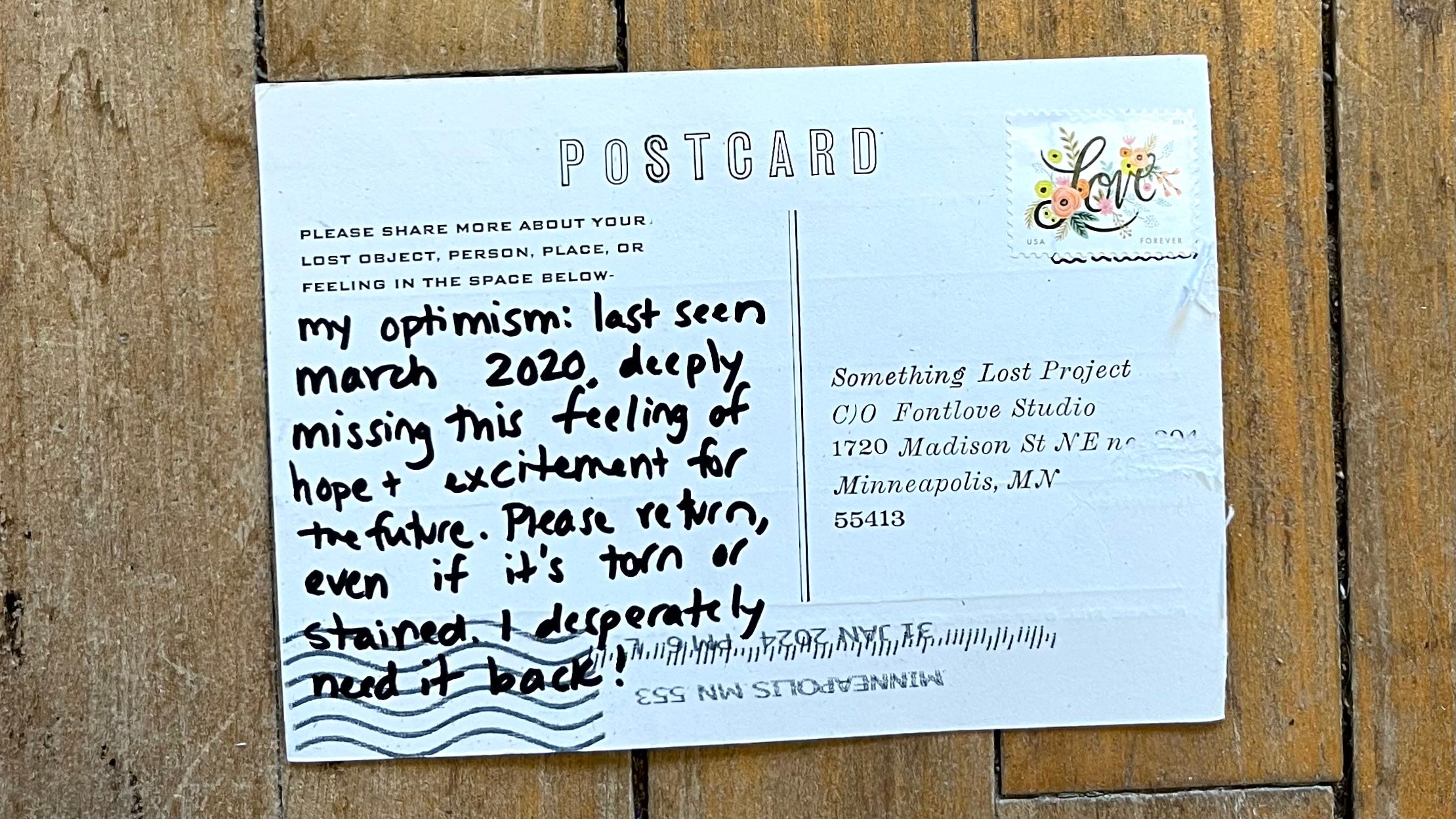 The back of the postcard. The left side says "Please share more about your lost object, person, place or feeling in the space below:" and it says in handwriting "my optimism: last seen march 2020, deeply missing this feeling of hope + excitement for the future. Please return, even if it's torn or stained. I desperately need it back!"