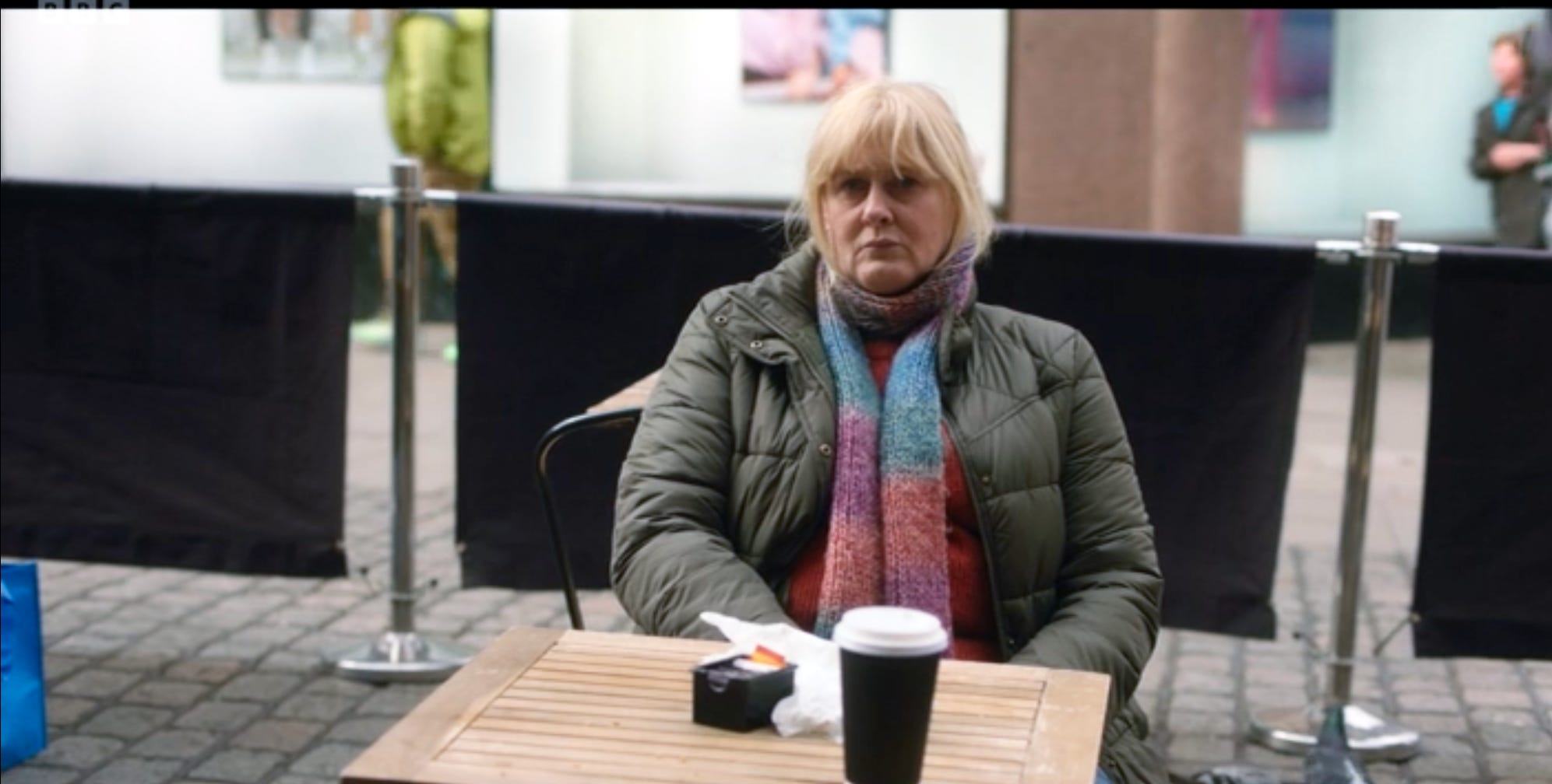 Sarah Lancashire, as Catherine in the drama, happy Valley, sitting looking despondent at an outdoor table at a café.