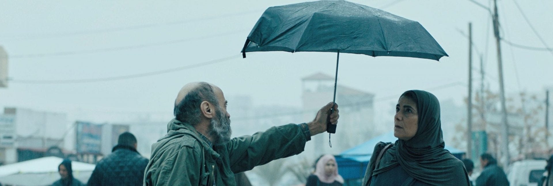 Il pescatore Issa porge un ombrello aperto alla sarta Siham in una piovosa giornata a Gaza. È l'immagine iconica del film Gaza Mon Amour.