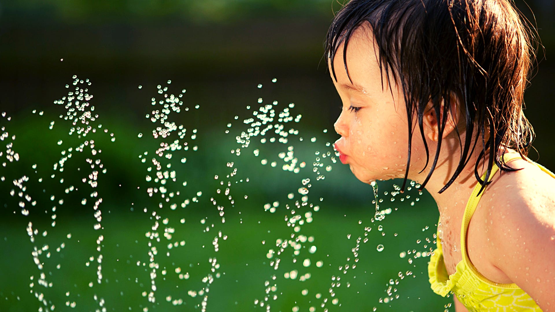 little child drinking from sprinkler
