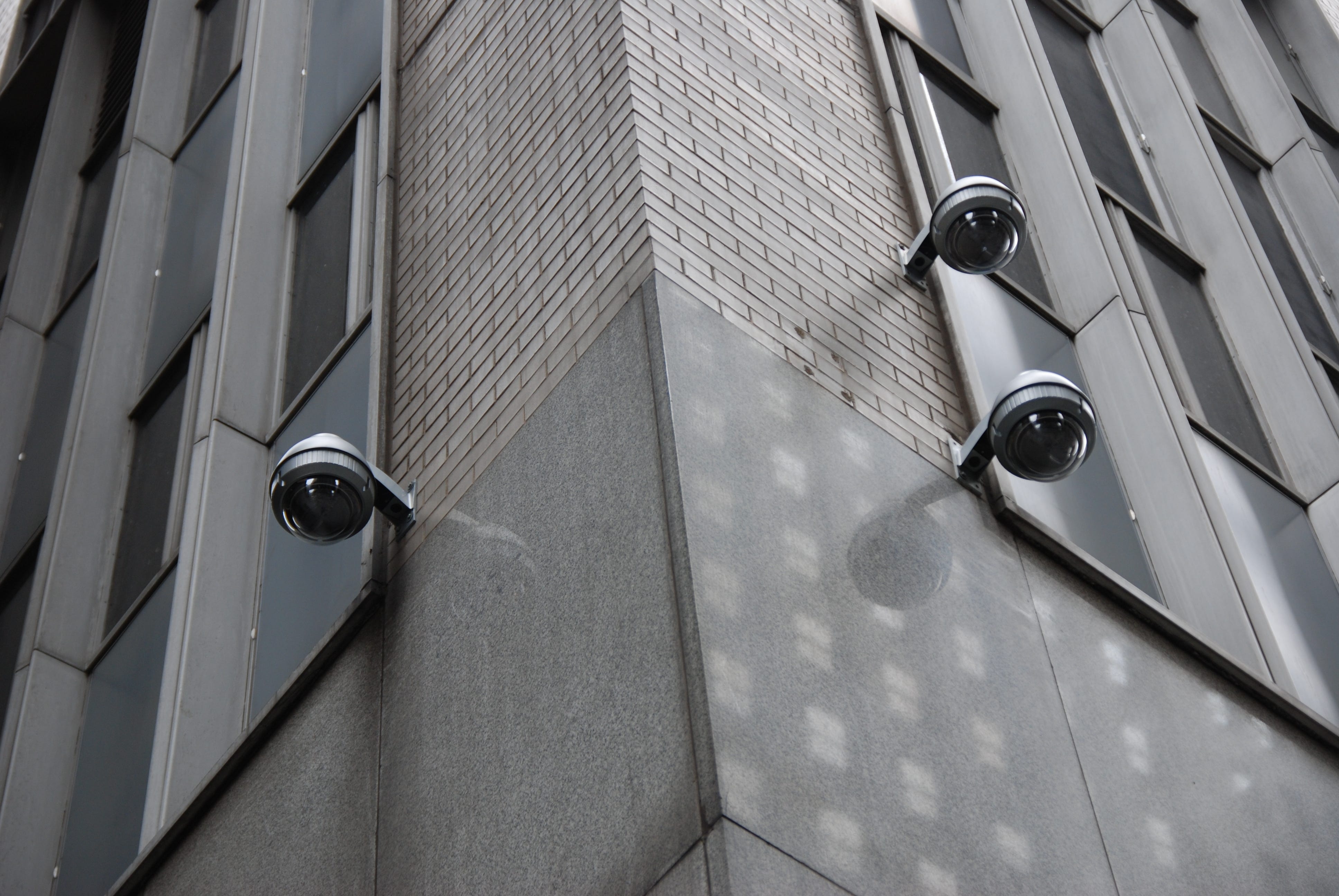 The corner of an urban building with three orb-shaped security cameras watching in all directions.