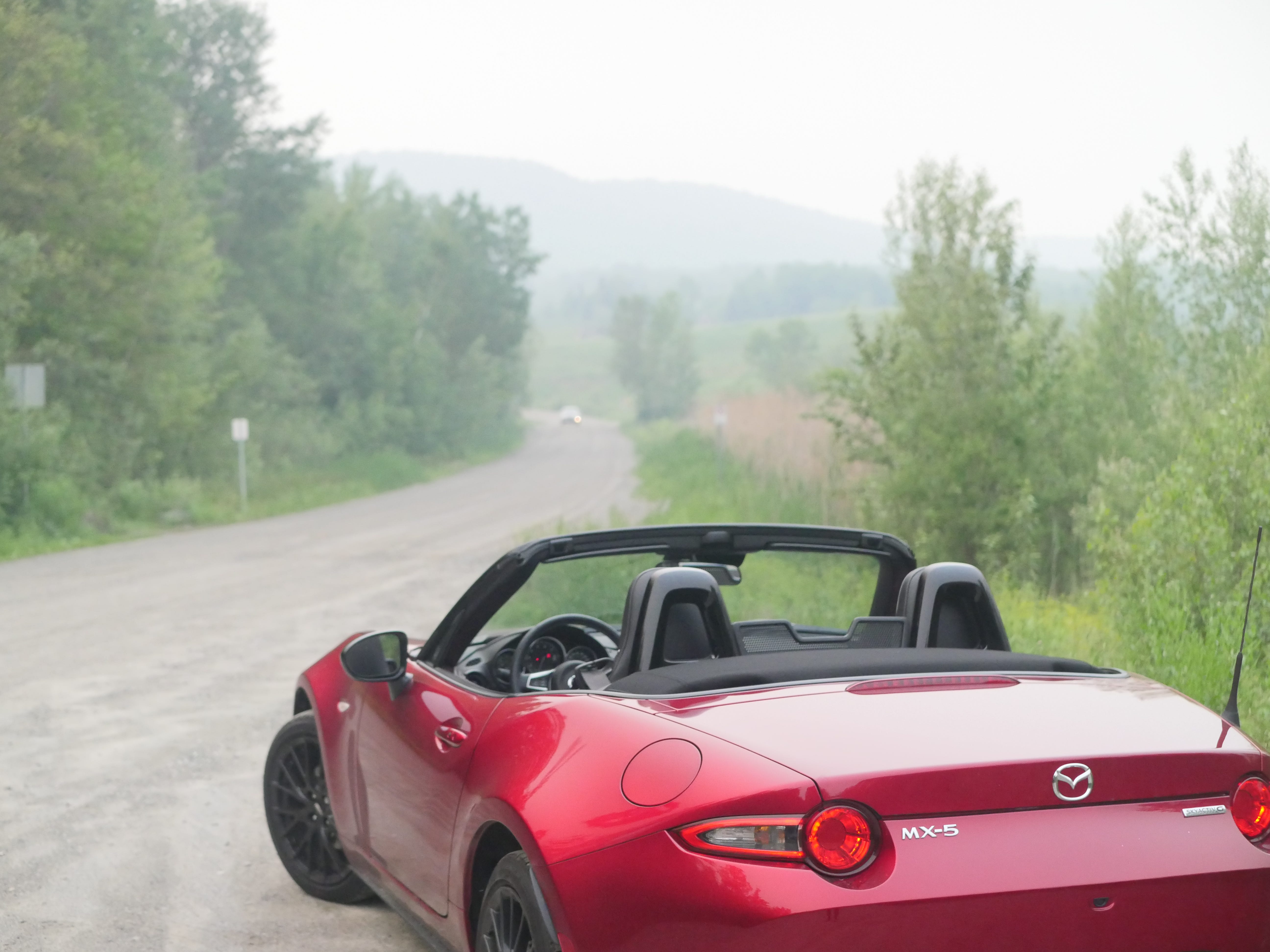 rear 3/4 of a 2023 mazda mx-5 miata roadster with hazy wildfire smog in the background