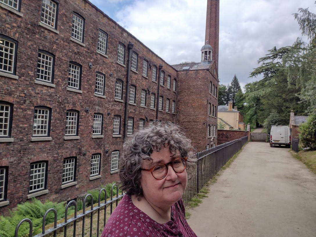Four story brick building with many identical windows and factory chimney, house glimpsed just beyond, Annette in photo