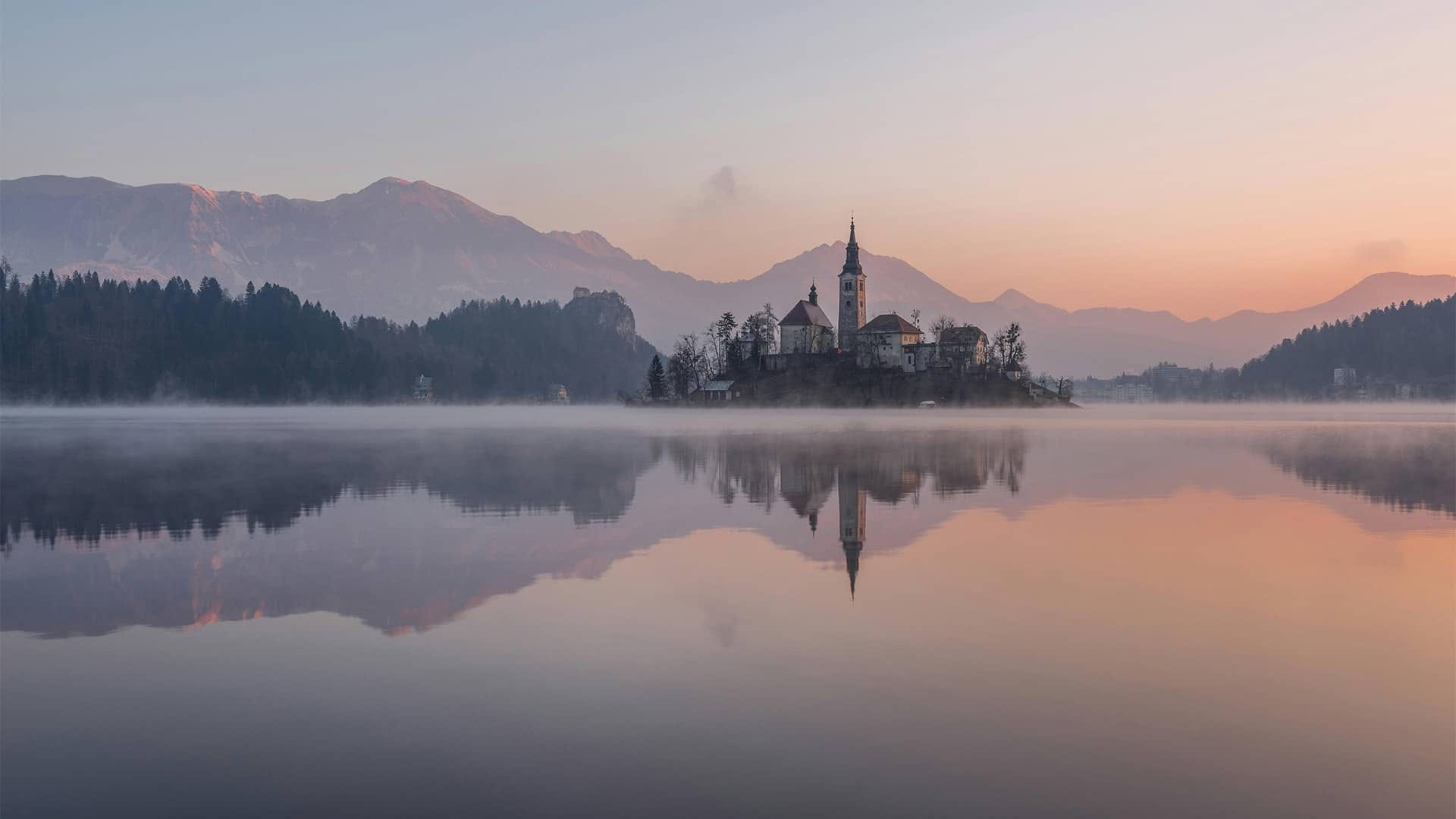 A lake perfectly mirroring a mountain, a forest, and a building.