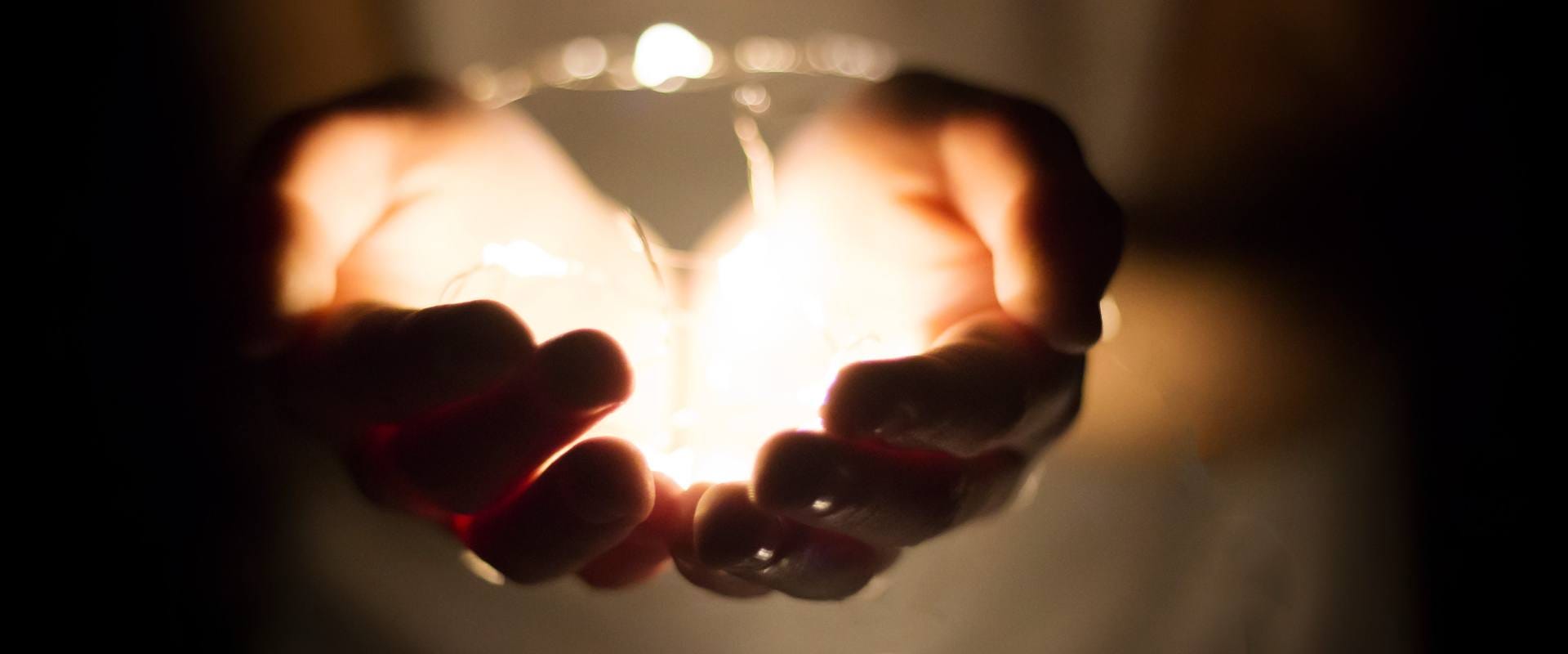 image of hands holding light in the darkness