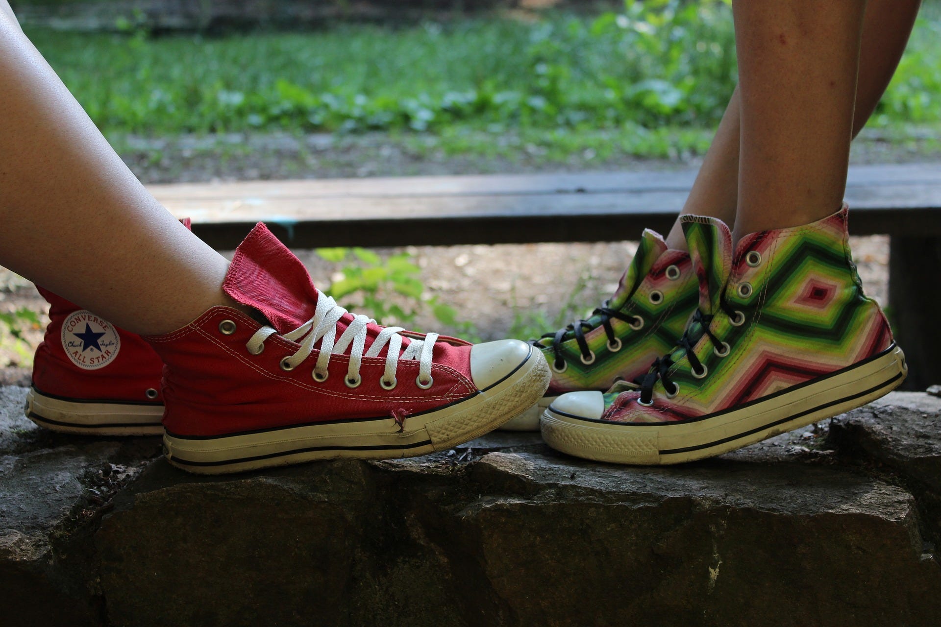 Two feet wearing canvas shoes of different colours facing each other.