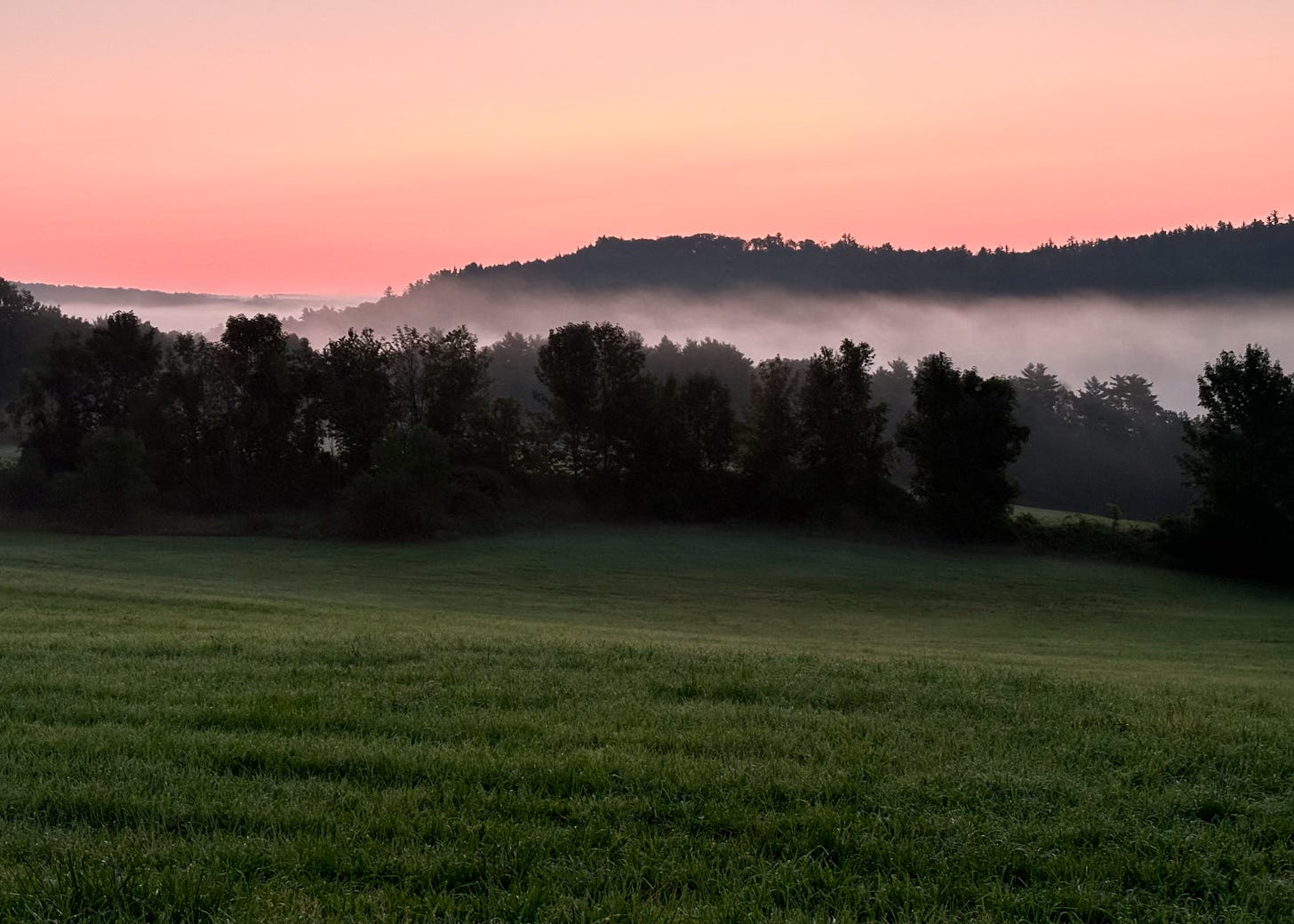 pink sunrise over dark foggy hills and meadow