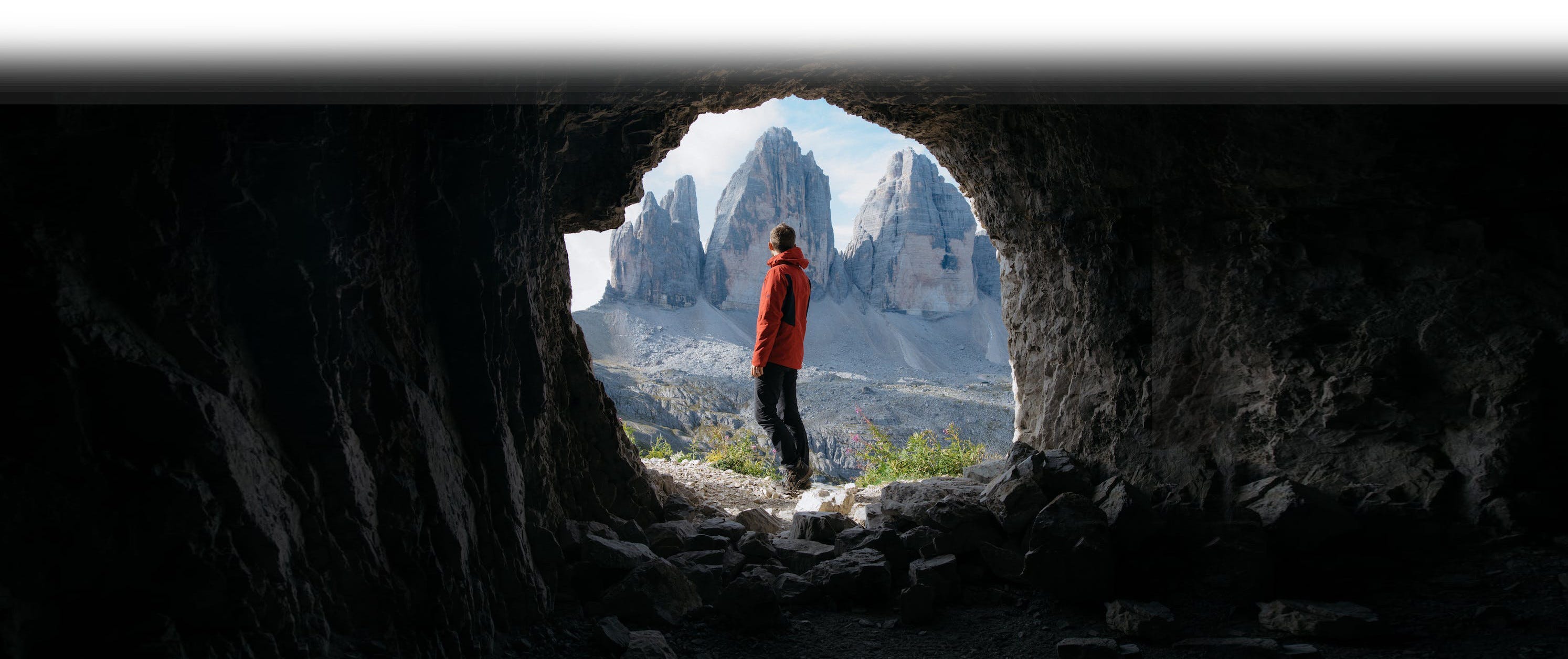 A man staring at a mountain range shot from inside a cave.