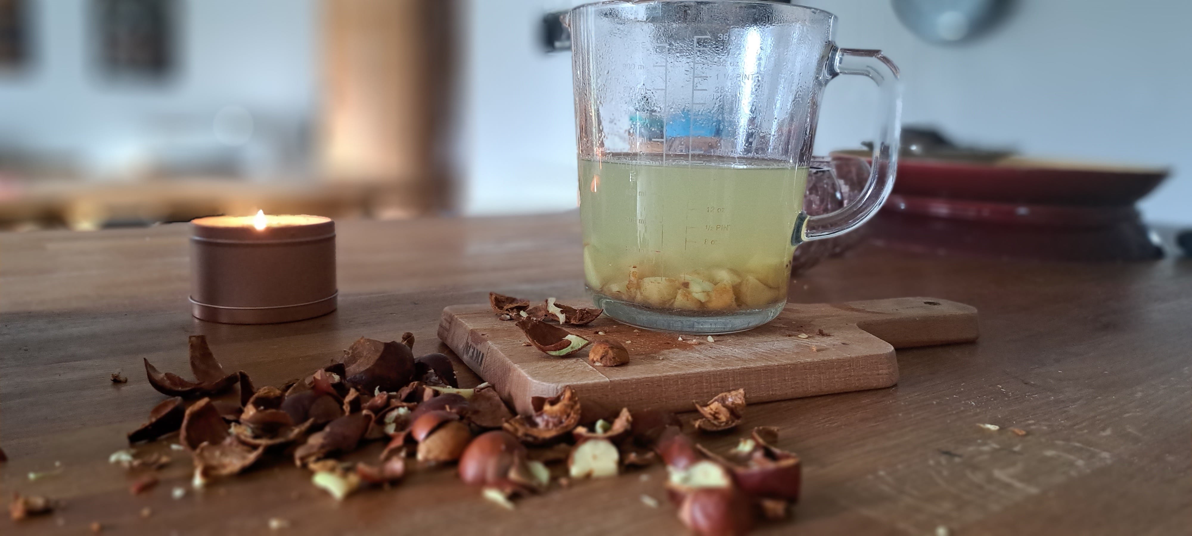 Glass jug sitting on the wooden worktop containing the chopped conkers with boiling water added; there is condensation on the walls of the jug.