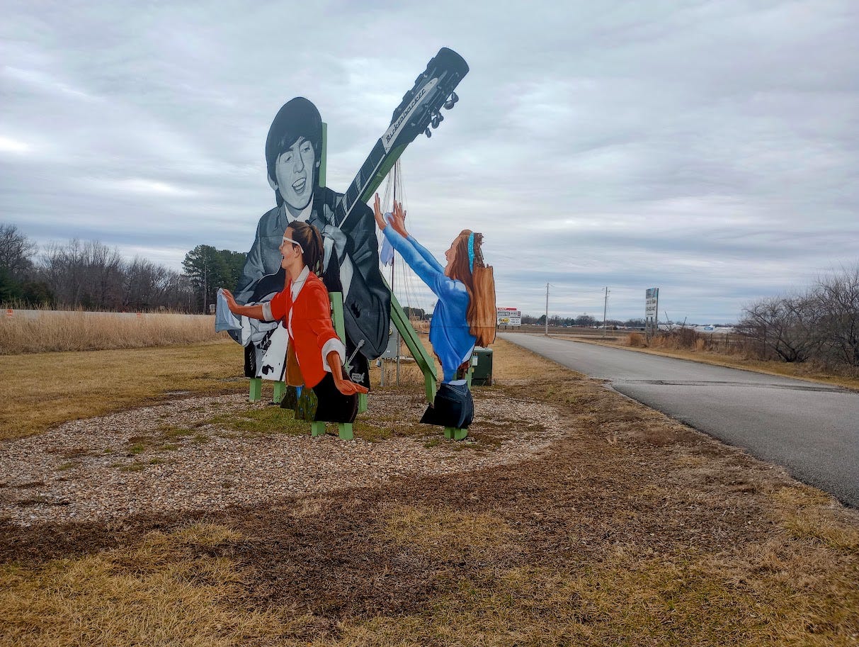 George Harrison with guitar and two screaming fans on cut-out billboard next to freeway and small airport