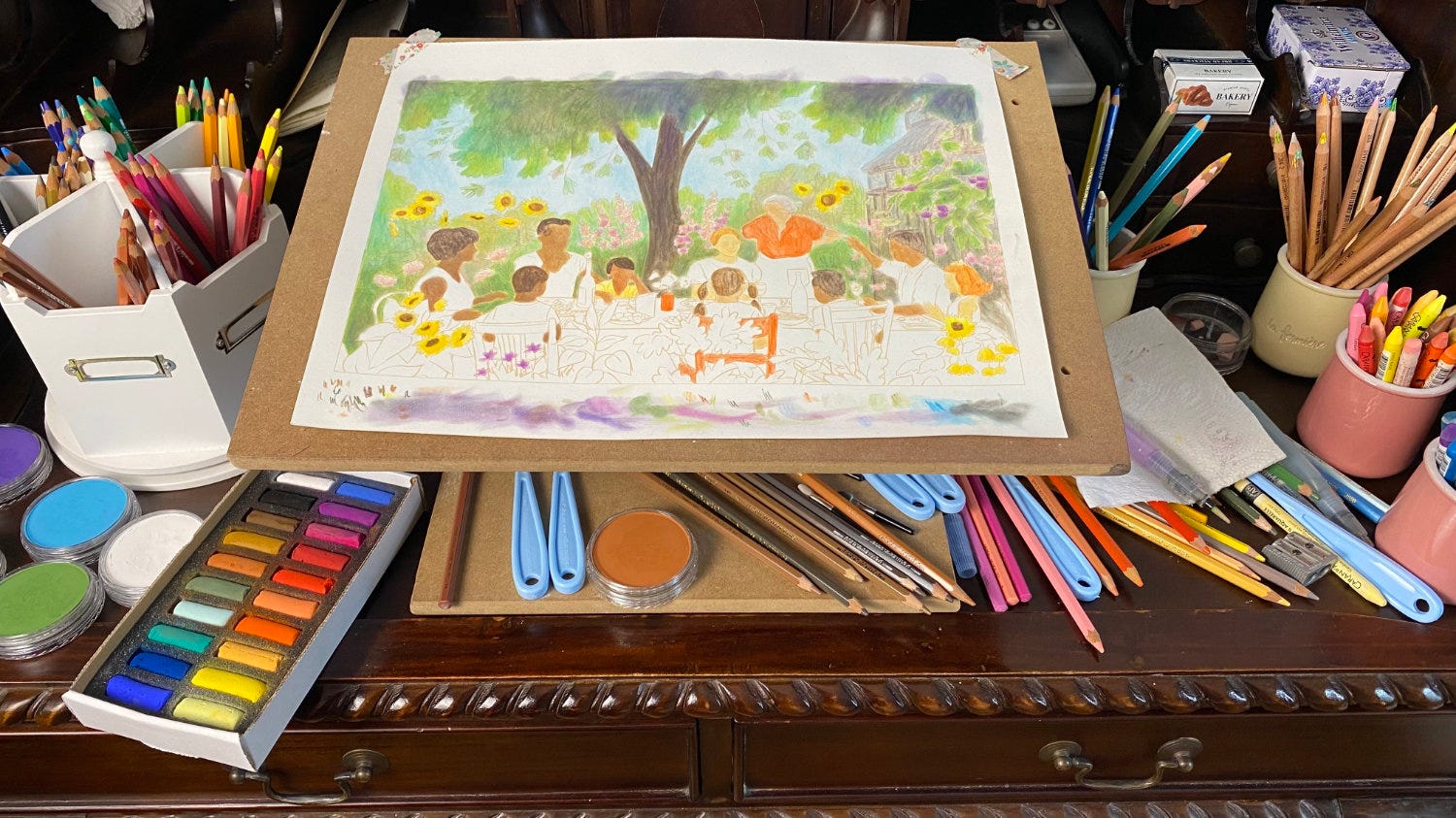 work in progress on a desk covered in pastels and colored pencils