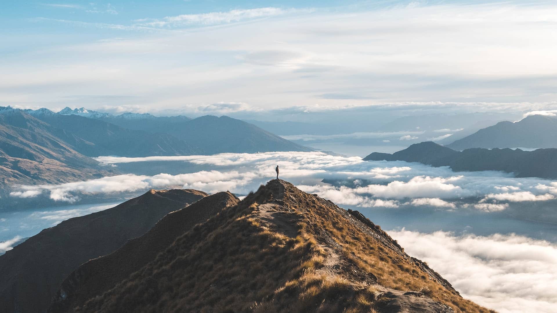 Person standing on top of a mountain above the clouds