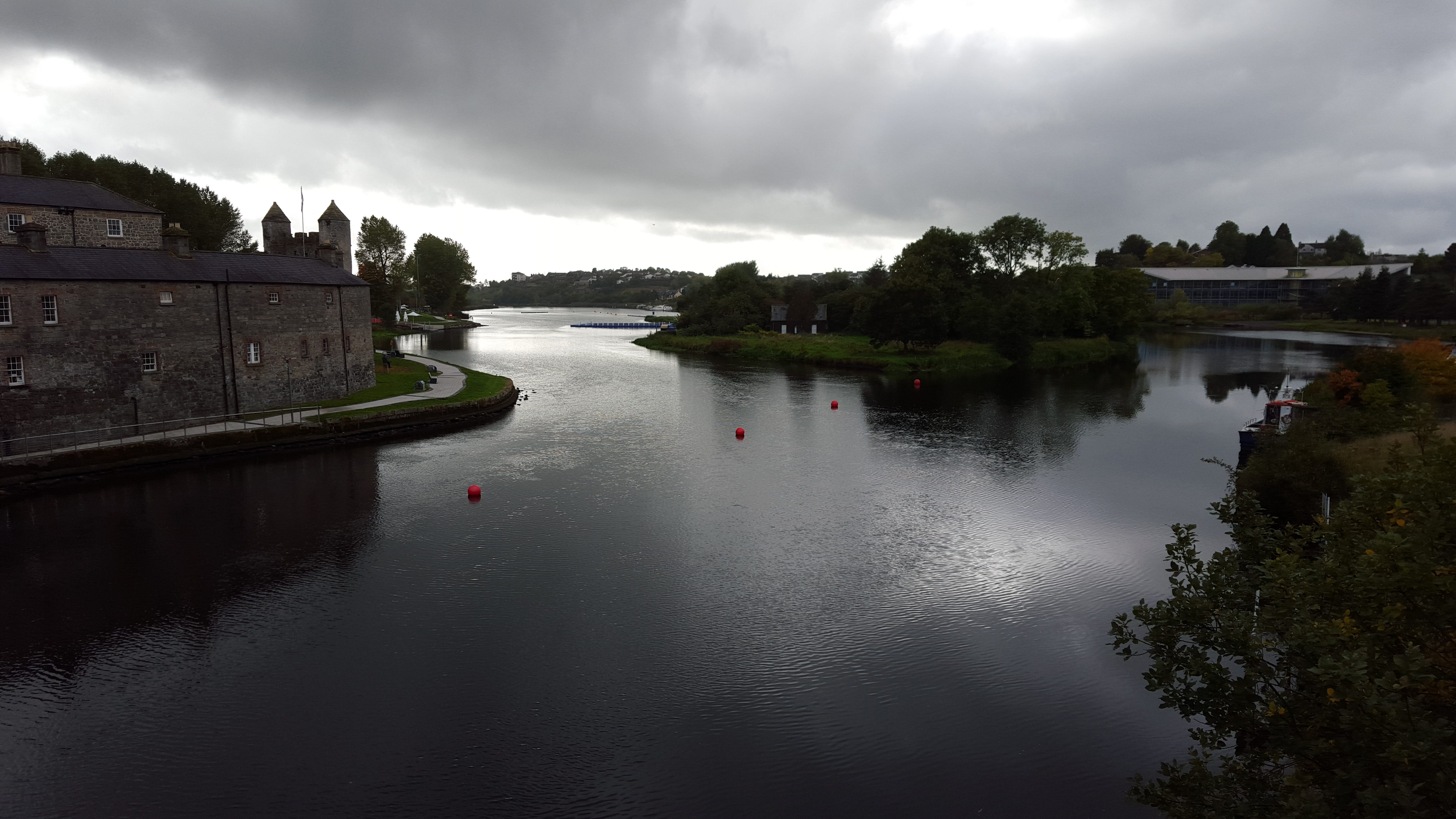 Picture of a river shin ing silver on a dark stormy day with low clouds in the sky and a rcastle to the left, with a river island to the right full of trees