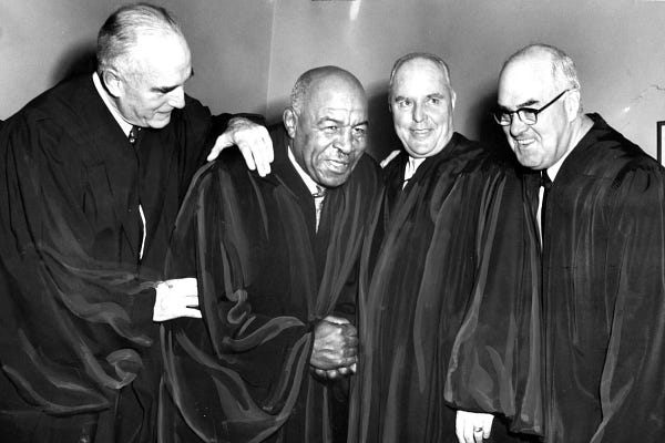 Duke Slater is surrounded by three colleagues, all of whom are wearing their black judicial robes.
