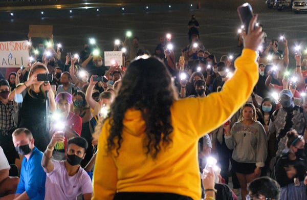 Cori Bush holds up her cell phone light in front of crowd all holding up their cell phone lights.