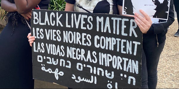 Photo of a handwritten protest sign that says BLACK LIVES MATTER in 5 different languages.