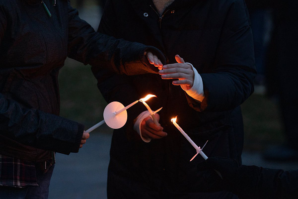 Two attendees of the candlelight vigil share a flame to ignite their candles.