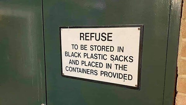 Sign says: REFUSE TO BE STORED IN BLACK PLASTIC SACKS AND PLACED IN THE CONTAINERS PROVIDED