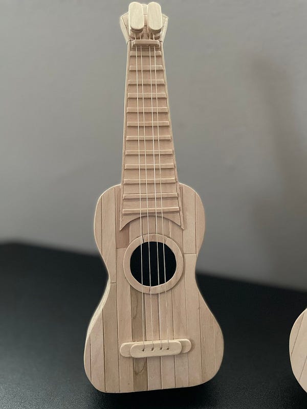 Picture of a ukulele against a black and gray background, made fully out of popsicles.