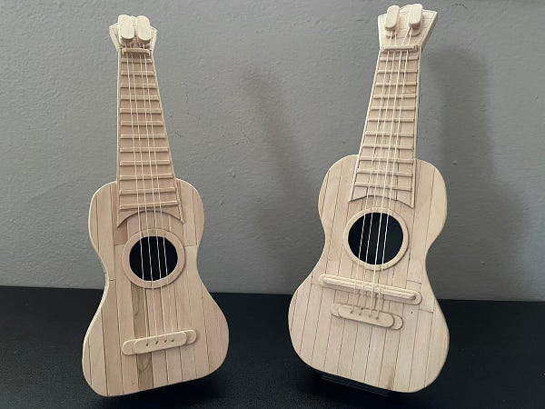 Picture of two wooden ukeleles against a black and gray background. They are made fully out of popsicles.