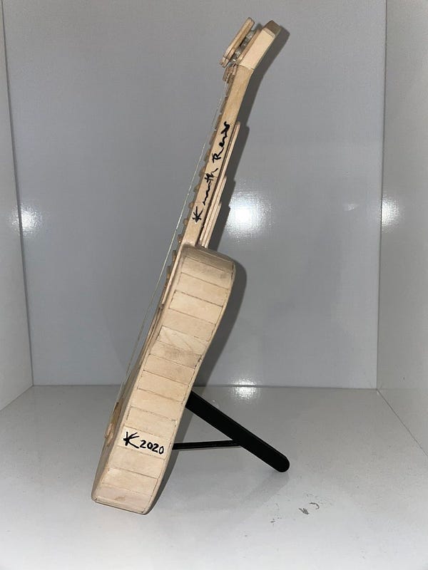 Picture of the side of a popsicle stick ukelele, showing Kenny Reams’ signature and that it was made in the year 2020.