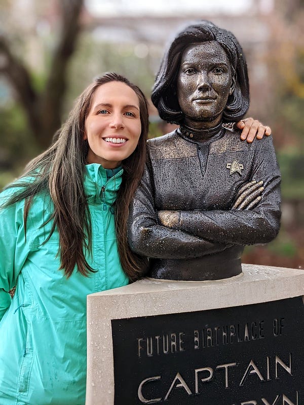 A woman stands with her arm around a statue of a Star Trek captain.