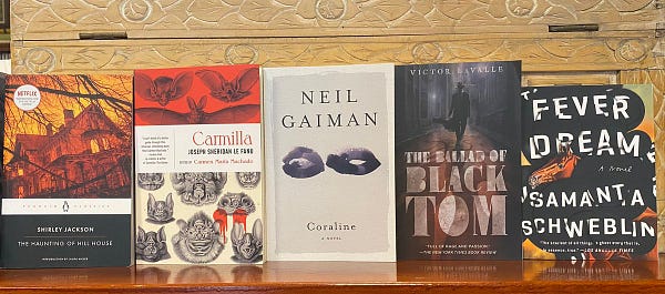 Books face out on a shelf: Jackson’s The Haunting of Hill House, Le Fanu’s Carmilla, Gaiman’s Coraline, LaValle’s The Ballad of Black Tom, and Schweblin’s Fever Dream.