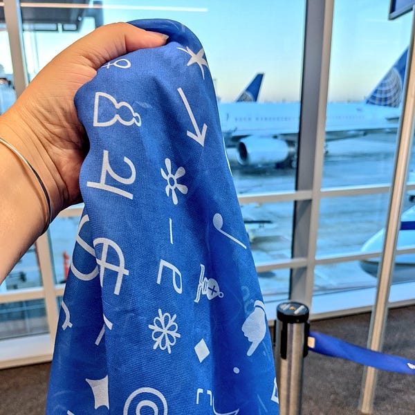 Esoteric characters scarf from Lingthusiasm, in light blue on medium blue, with some airplane tails in the background