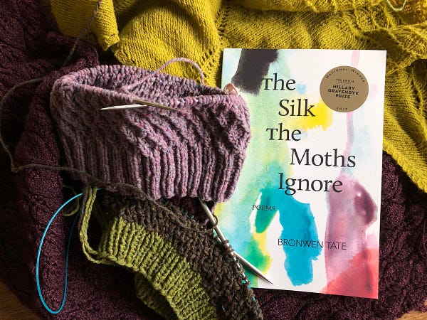 Bronwen Tate's book, The Silk the Moths Ignore, is surrounded by handknit shawls and hats. Colors are mostly yellow, purple, lavender. 