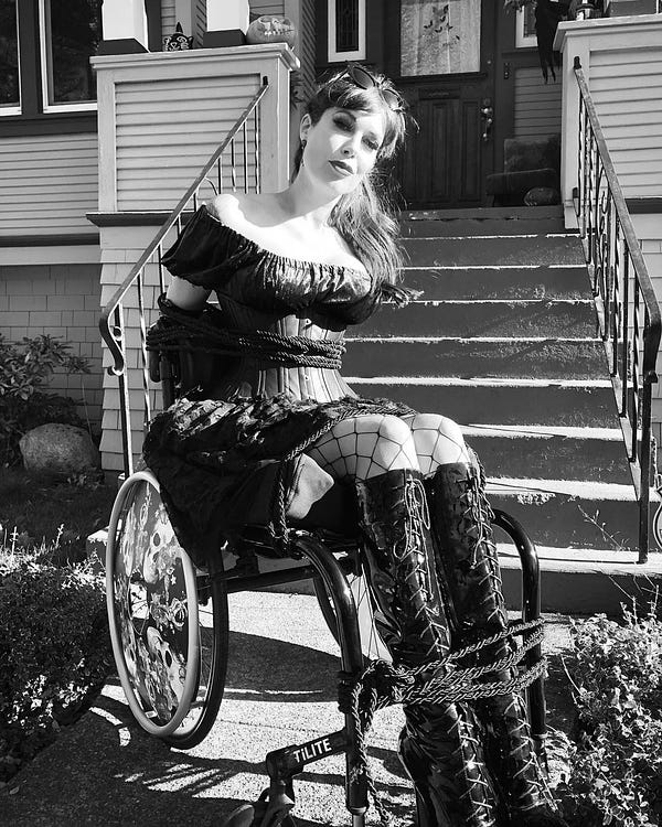 ID: Tara is a disabled woman with CRPS, using her rockin’ wheelchair. For Halloween she is faux bound to her wheelchair with rope.