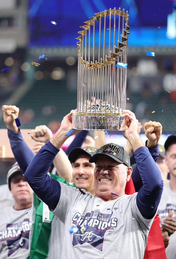 Brian Snitker smiles as he holds up the 2021 World Series trophy.