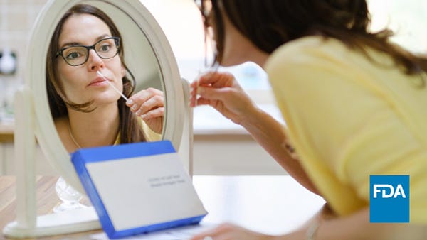 A woman uses a nasal swab on herself while looking in the mirror.