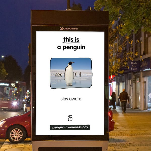 Our first advert for this year's Penguin Awareness Day. This one is on an advertising hoarding in the middle of a town centre. The hoarding has the writing "This is a penguin" and then there is a picture of a penguin. Underneath it, it reads "stay aware". And then right at the bottom it says Penguin Awareness Day.