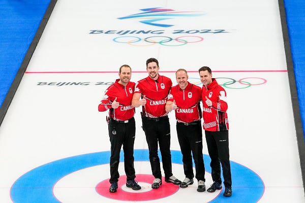 A photo of four men on curling ice smiling giving a thumbs up
