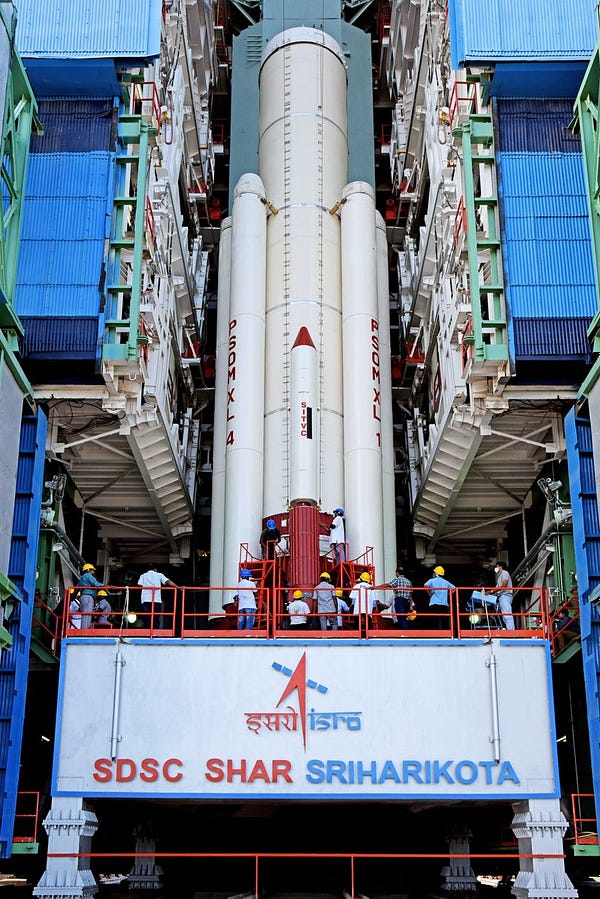 Multiple strap-on rockets attached around the side of the central solid rocket booster. The text on the platform says SDSC SHAR Sriharikota.