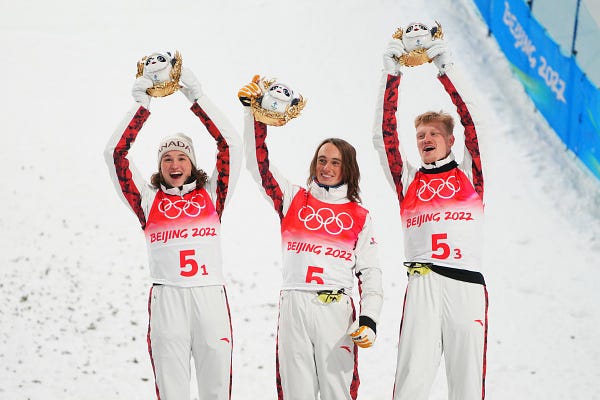 Three athlete stand on the podium raising their hands in the air. 