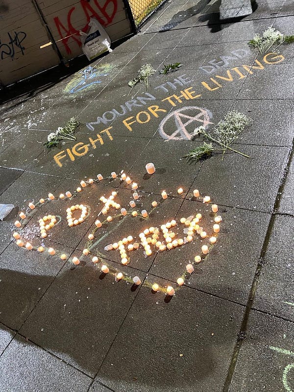 Two large hearts made out of tea light candles stacked on top of one another. The middle of the first heart spells out “pdx” in candles and the second heart spells out “T-REX” in candles. It’s surrounded by messages, one reads “mourn the dead fight for the living!”