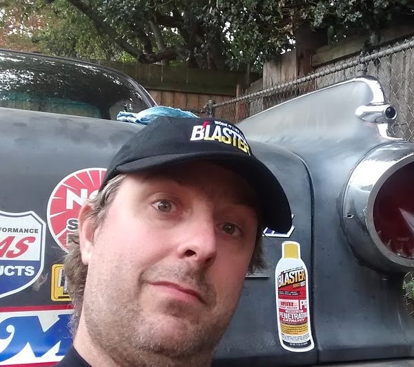 Mass shooter Benjamin Jeffrey Smith posing in front of a classic car wearing a black cap that says blaster.