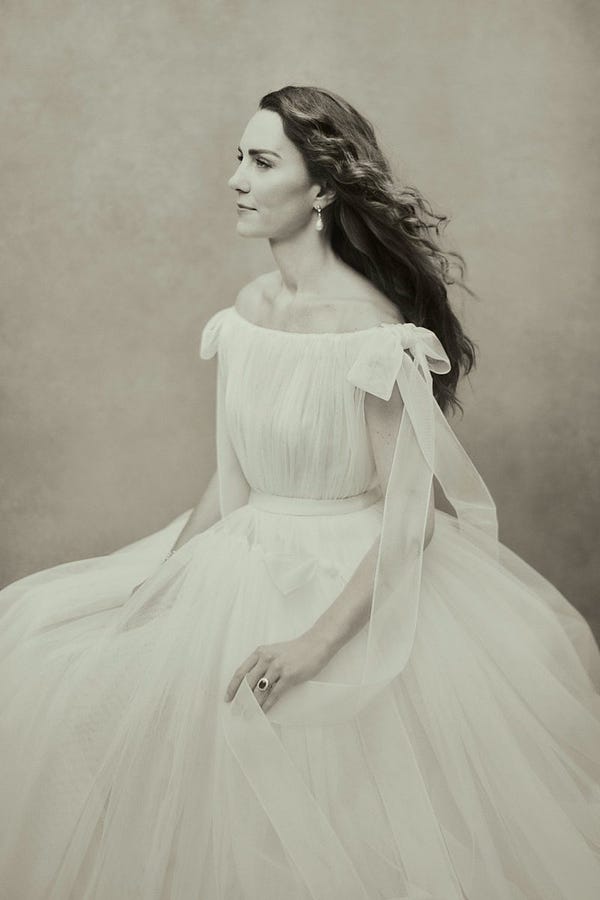 A sepia tone photograph of The Duchess of Cambridge, seated, looking to her right. Her hair is blowing behind her. Her wedding ring can be seen on her left hand.