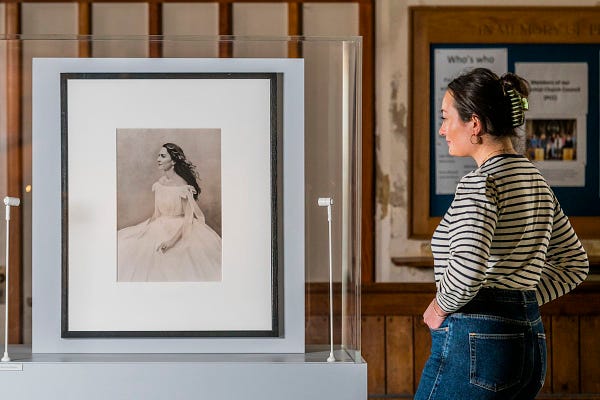 A photograph of a woman looking at a portrait of The Duchess of Cambridge in a glass case.