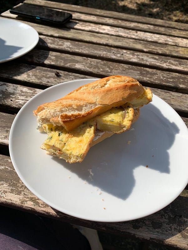 A delicious Spanish tortilla sandwich in a half a crusty baguette. It is on a garden table on a sunny day.