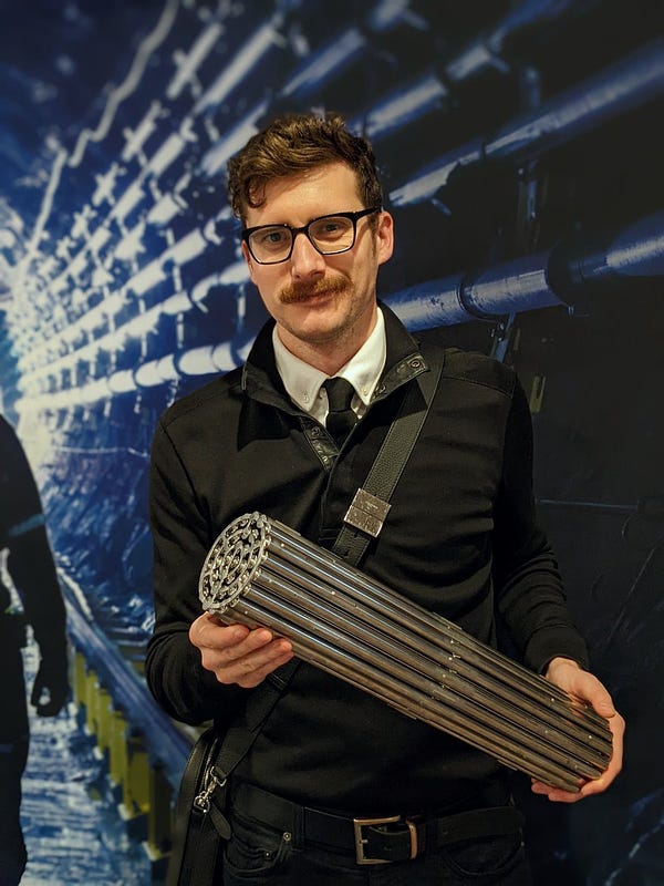 a guy trying not to smile too hard while holding a shiny silver nuclear reactor fuel bundle