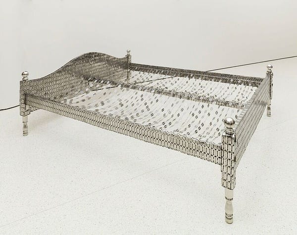 Photograph of a sculpture in the shape of a double bed frame covered in stainless steel razor blades, with wires evenly draped across the width of the bed with razor blades attached, in a plain white room