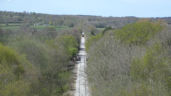 Aerial view of the restoration of the Dartmoor Line. A train travels along the line in the distance on a sunny day.