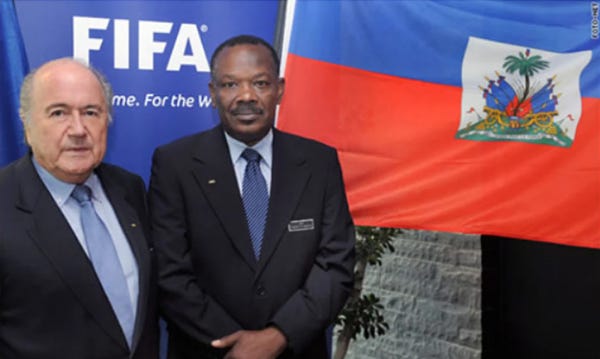 Sepp Blatter, presidente da FIFA, e Yves Jean-Bart, presidente da federação de futebol do Haiti, posam para foto lado a lado. Ao fundo, as bandeiras da FIFA e do Haiti.