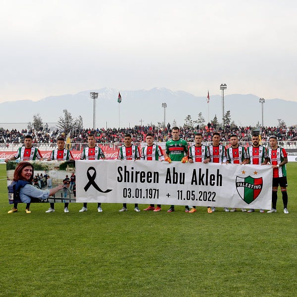 Equipe do Palestino, clube chileno, perfilada segurando uma faixa com o nome de Shireen Abu Akleh, sua data de nascimento (3/1/1971) e sua data de morte (11/5/2022). Além disso, há a foto dela à esquerda e o símbolo do clube à direita da faixa.