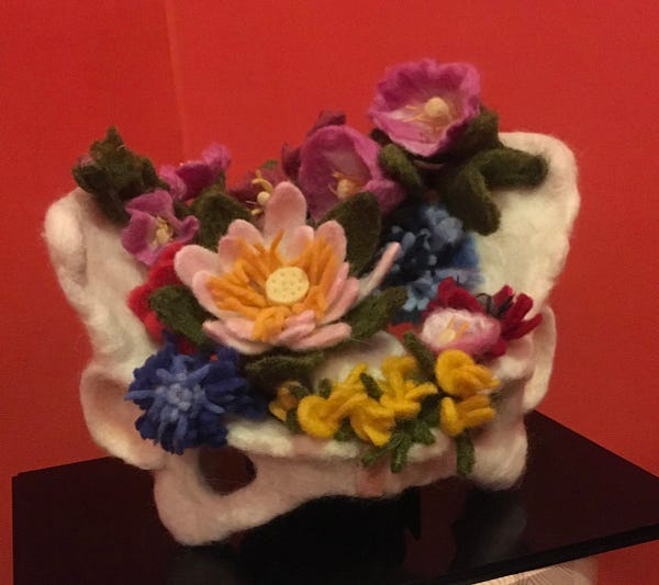 Felt sculpture of a bony pelvis with an array of colourful flowers sitting in the false pelvis